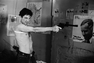 Roberto De Niro as Travis Bickle in the movie Taxi Driver, pointing his gun at the mirror in one of the most iconic cinematic scenes “You Talkin’ to me”